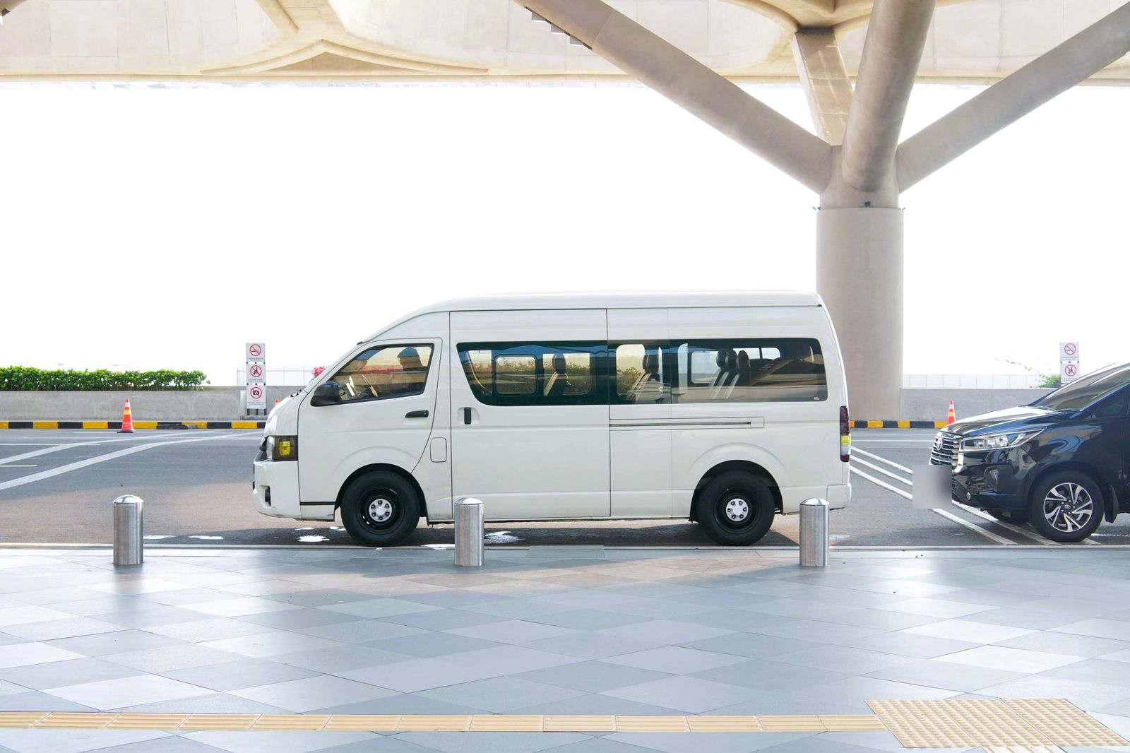 A white passenger van waiting at an airport curb