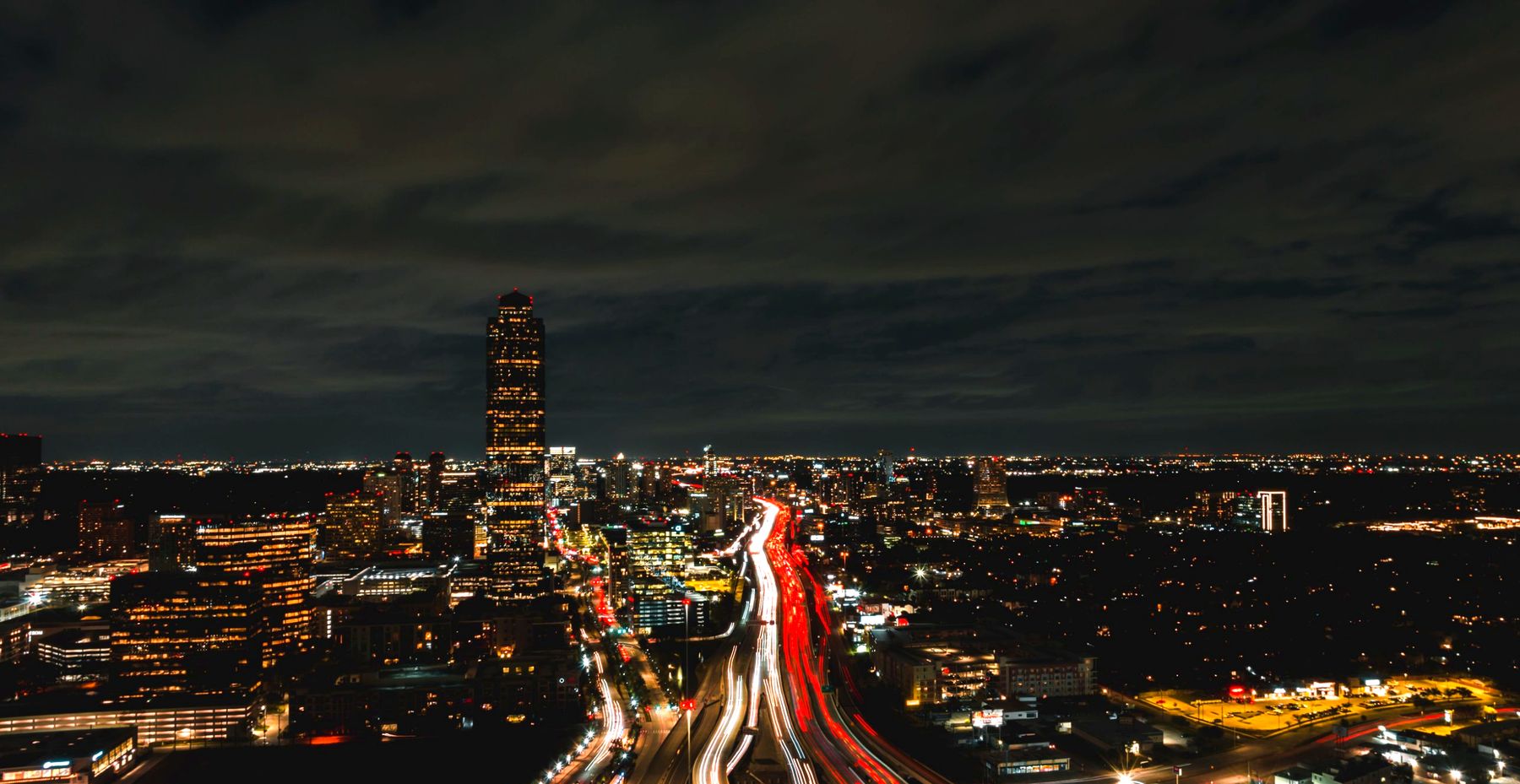 Houston at night, with light trails on the freeway below a lit tower