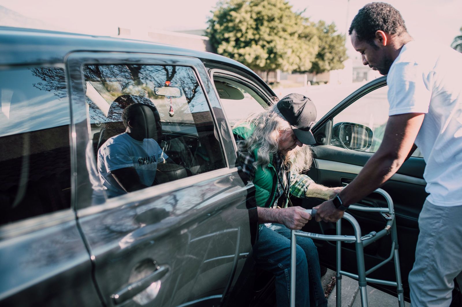 A driver steadies a walker as an older man steps out of a car
